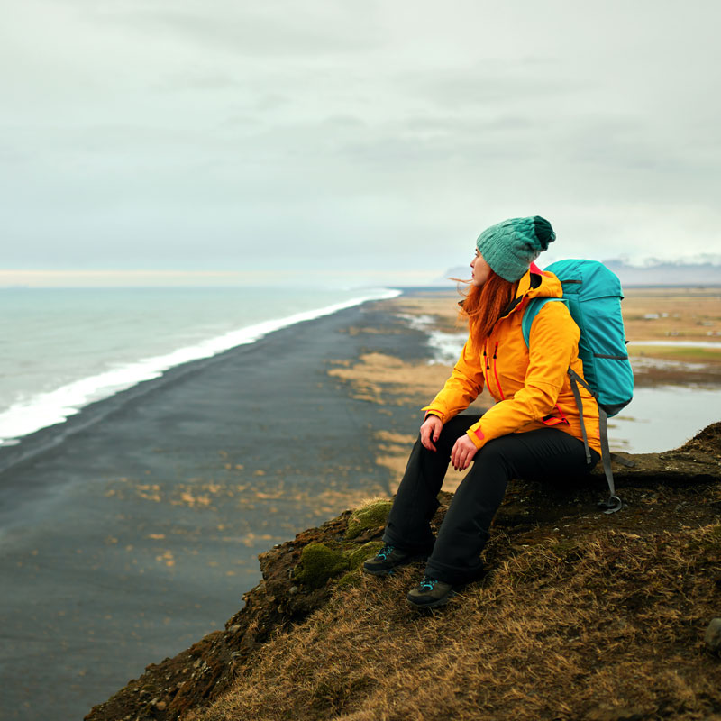 Woman sitting on mountain cliff and watching ocean